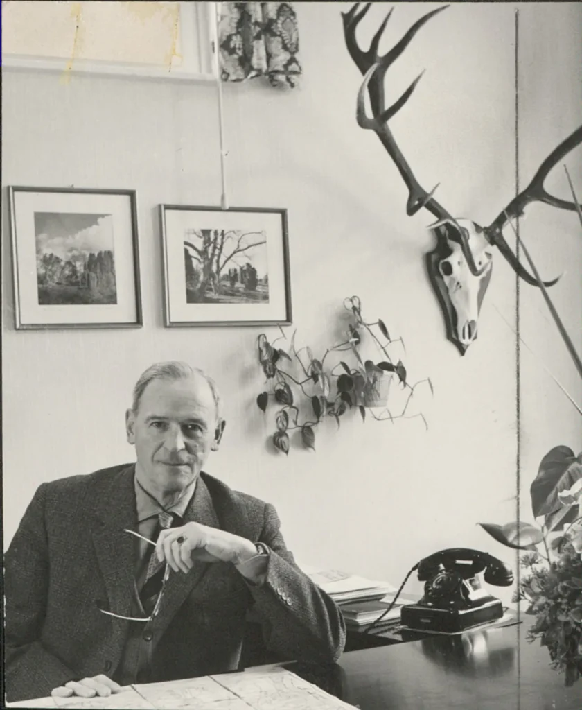 Johann Dietrich Lauenstein sitzt an seinem Schreibtisch mit Telefon, im Hintergrund Gemälde und ein Hirschgeweih.