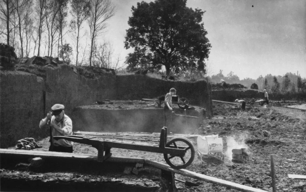 Arbeiter stechen und verarbeiten Torf in einem Hochmoor, mit Schienen und Gerät im Vordergrund.