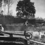 Arbeiter stechen und verarbeiten Torf in einem Hochmoor, mit Schienen und Gerät im Vordergrund.