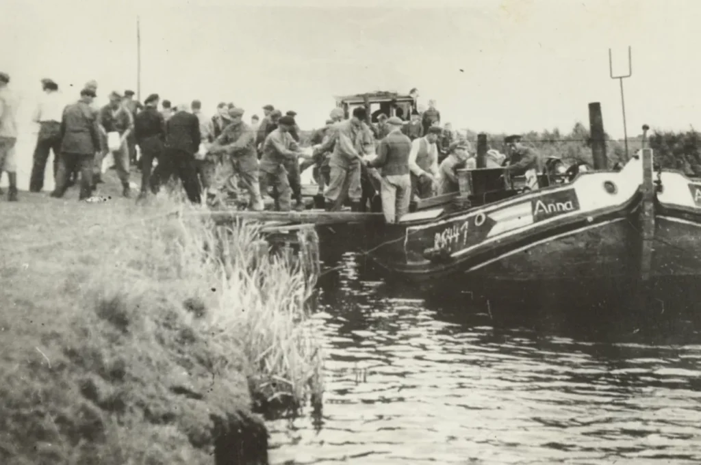 Mehrere Menschen entladen ein Lastboot namens Anna an einem Kanalufer, vermutlich Flüchtlinge bei der Ankunft, 1940er Jahre.