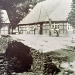 Schwarzweißfoto eines Fachwerkgehöfts mit Sandweg und Trockensteinmauer im ländlichen Emsland um 1950.