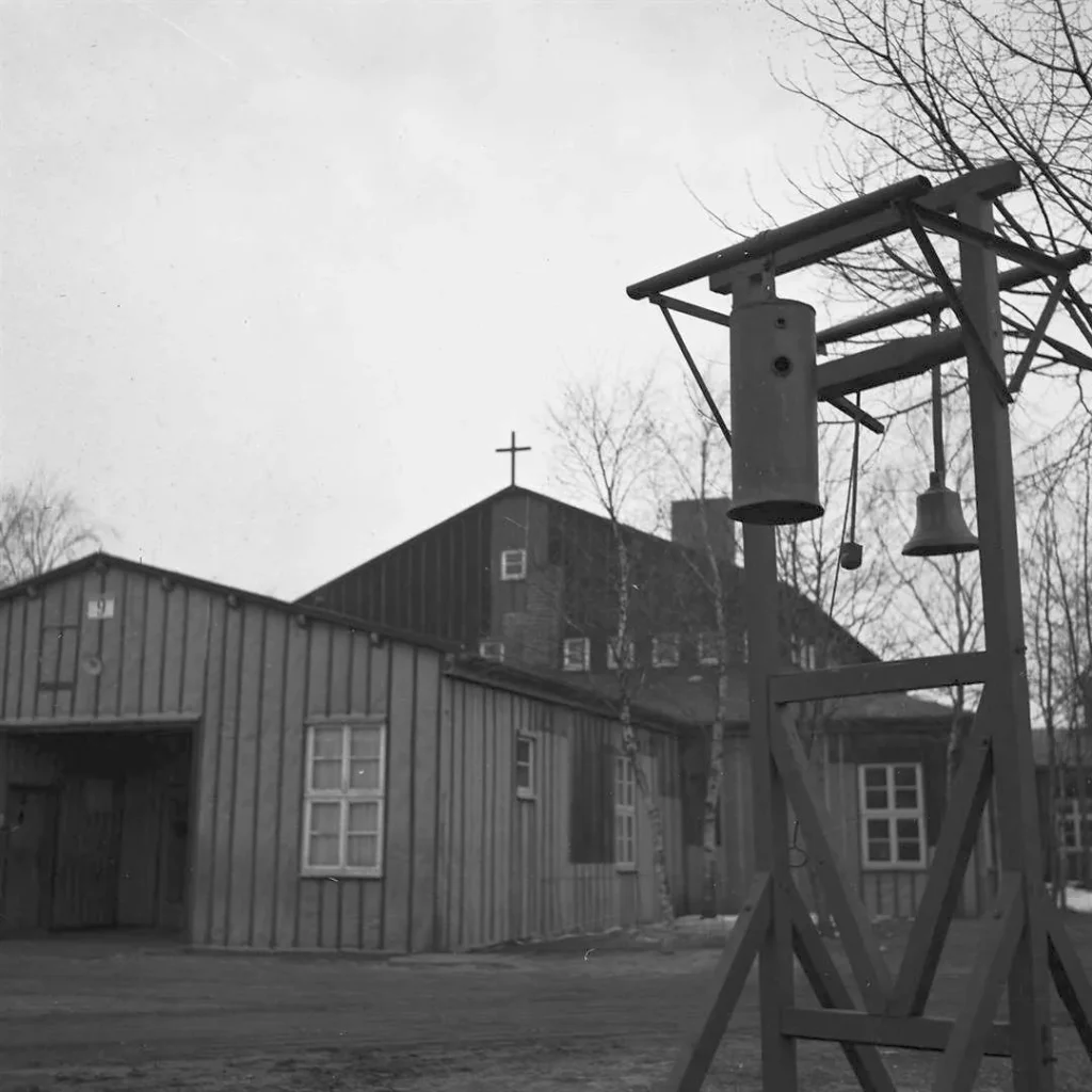 Blick auf hölzerne Baracken mit Kreuz und einem Glockenturm im Flüchtlingslager Neugnadenfeld, 1946.