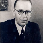 Schwarzweißes Porträtfoto eines älteren Mannes mit runder Brille und dunklem Anzug aus der Nachkriegszeit.
