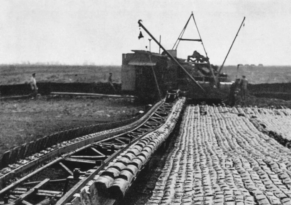 Historische Schwarzweißaufnahme eines Schaufelradbaggers beim Moorabbau auf Schienen im Emsland, umgeben von Arbeitern.