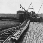 Historische Schwarzweißaufnahme eines Schaufelradbaggers beim Moorabbau auf Schienen im Emsland, umgeben von Arbeitern.