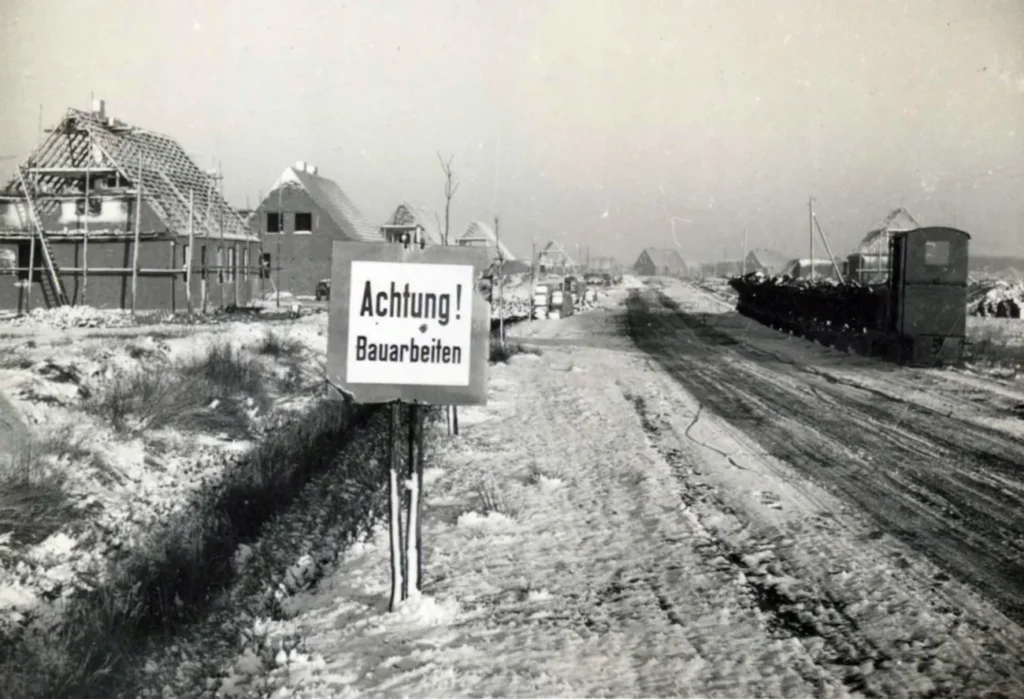 Verschneite Baustelle mit Rohbauten und Warnschild 'Achtung Bauarbeiten' beim Aufbau der Flüchtlingssiedlung Neugnadenfeld.