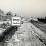 Verschneite Baustelle mit Rohbauten und Warnschild 'Achtung Bauarbeiten' beim Aufbau der Flüchtlingssiedlung Neugnadenfeld.
