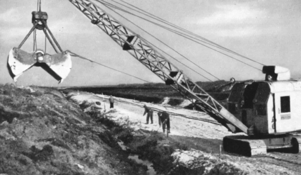 Ein Dragline-Bagger hebt Torfmassen im Emsland aus, während Arbeiter die Entwässerungsarbeiten begleiten.