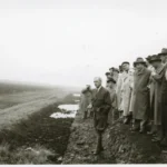 Gruppe von Männern in Mänteln besichtigt ein entwässertes Emslandmoor, ein Mann zeigt in die Ferne.