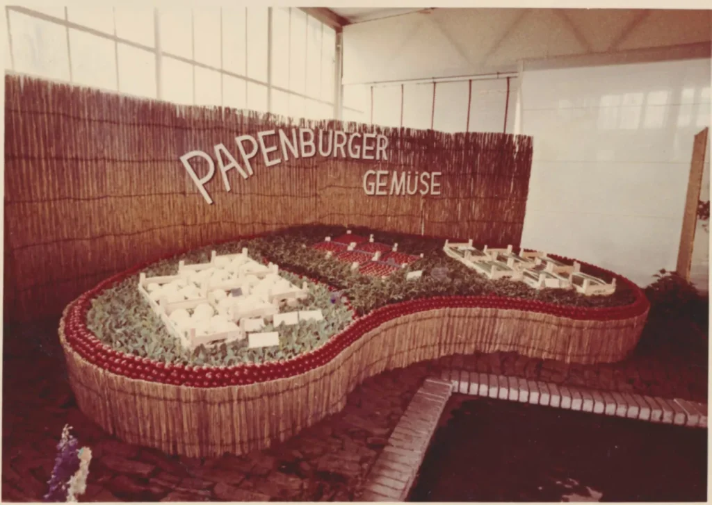 Ausstellungsstand der Papenburger Gemüsegenossenschaft mit Modell, Tomatenrand und Schriftzug 'Papenburger Gemüse' auf Bambushintergrund.