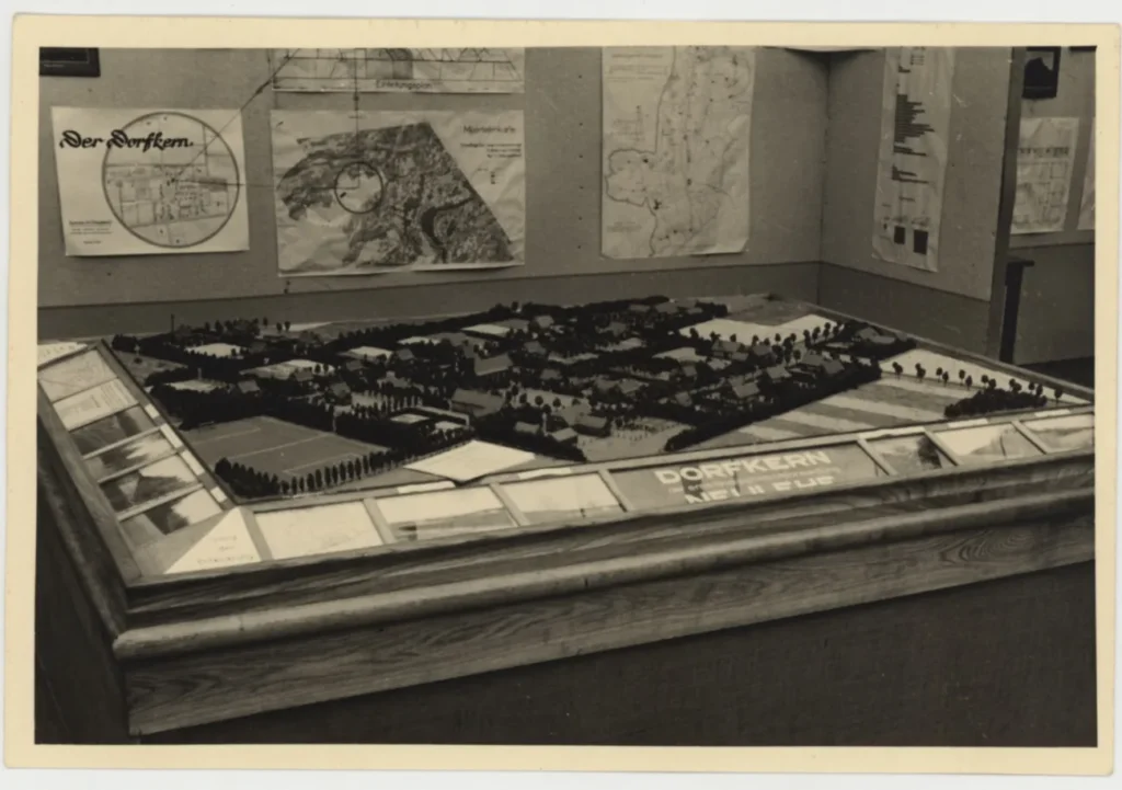 Architektonisches Stadtmodell eines Dorfkerns auf einem Tisch, umgeben von Karten und Plänen der Emslandausstellung 1951.