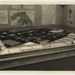 Architektonisches Stadtmodell eines Dorfkerns auf einem Tisch, umgeben von Karten und Plänen der Emslandausstellung 1951.