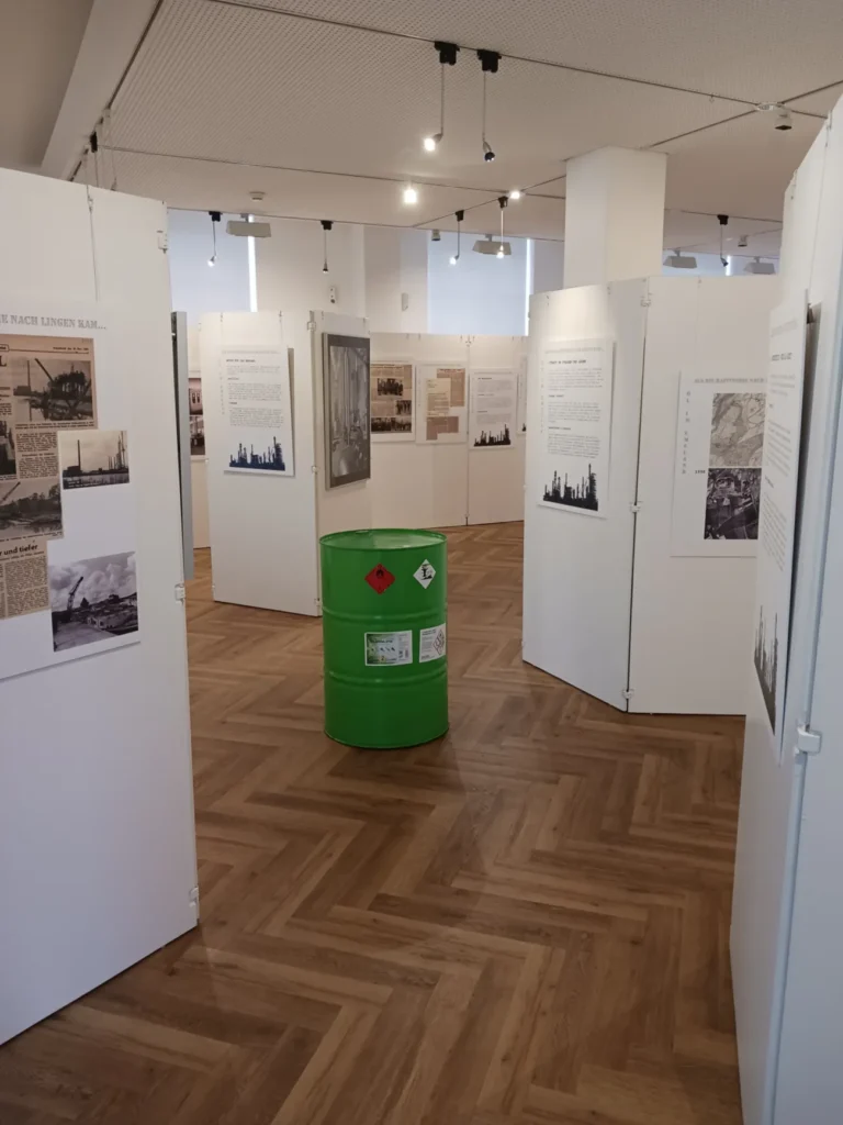 Museumsraum mit historischen Tafeln und grünem Ölfass als Ausstellungsobjekt zur Geschichte der Lingener Raffinerie.