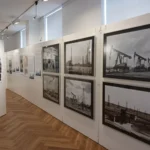 Museumsgang mit historischen Schwarzweißfotos von Ölförderanlagen und Pumpen zur Geschichte der Lingener Raffinerie.
