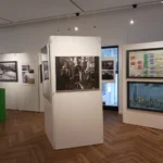Museumsausstellung mit historischen Schwarz-Weiß-Fotos von Arbeitern, Industriediagrammen und einem grünen Ölfass.