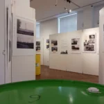 Museumsraum mit historischen Schwarz-Weiß-Fotos zur Raffineriegeschichte Lingens, im Vordergrund grünes Ölfass.