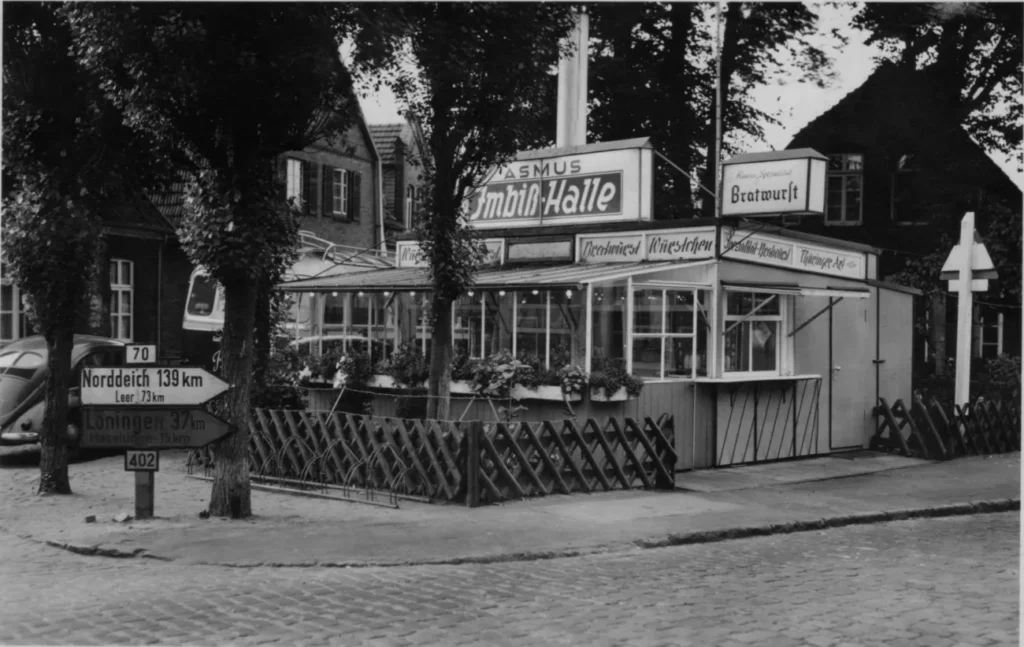 Historische Aufnahme der Asmus Imbiß-Halle in Meppen mit Straßenschildern nach Norddeich und Löningen, ca. 1950er Jahre.