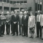 Elf Personen in formeller Kleidung stehen vor einem modernen Backsteingebäude bei der Auflösungsfeier der Emsland GmbH.