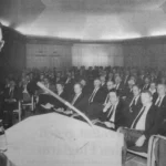 Ein Redner spricht vor einem vollbesetzten Saal mit Anzugträgern bei der Abschlussfeier der Emsland GmbH.