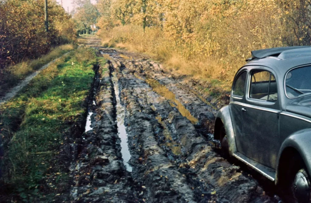 Ein grauer VW Käfer steht auf einem tief aufgewühlten, matschigen Feldweg in der Grafschaft Bentheim, ca. 1950er Jahre.