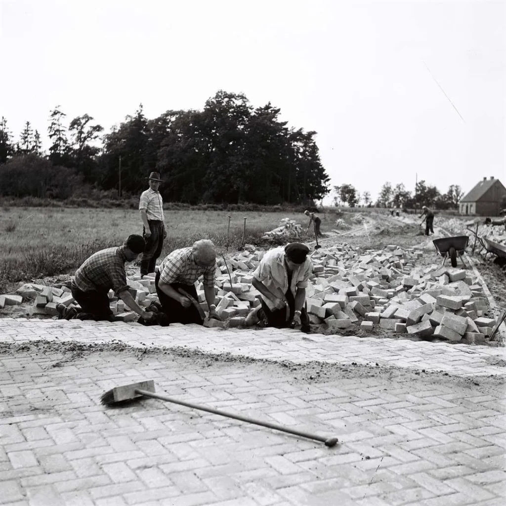 Arbeiter verlegen händisch Kopfsteinpflaster auf einer neu angelegten Straße in der Grafschaft Bentheim, 1950er Jahre.