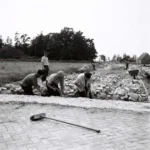 Arbeiter verlegen händisch Kopfsteinpflaster auf einer neu angelegten Straße in der Grafschaft Bentheim, 1950er Jahre.