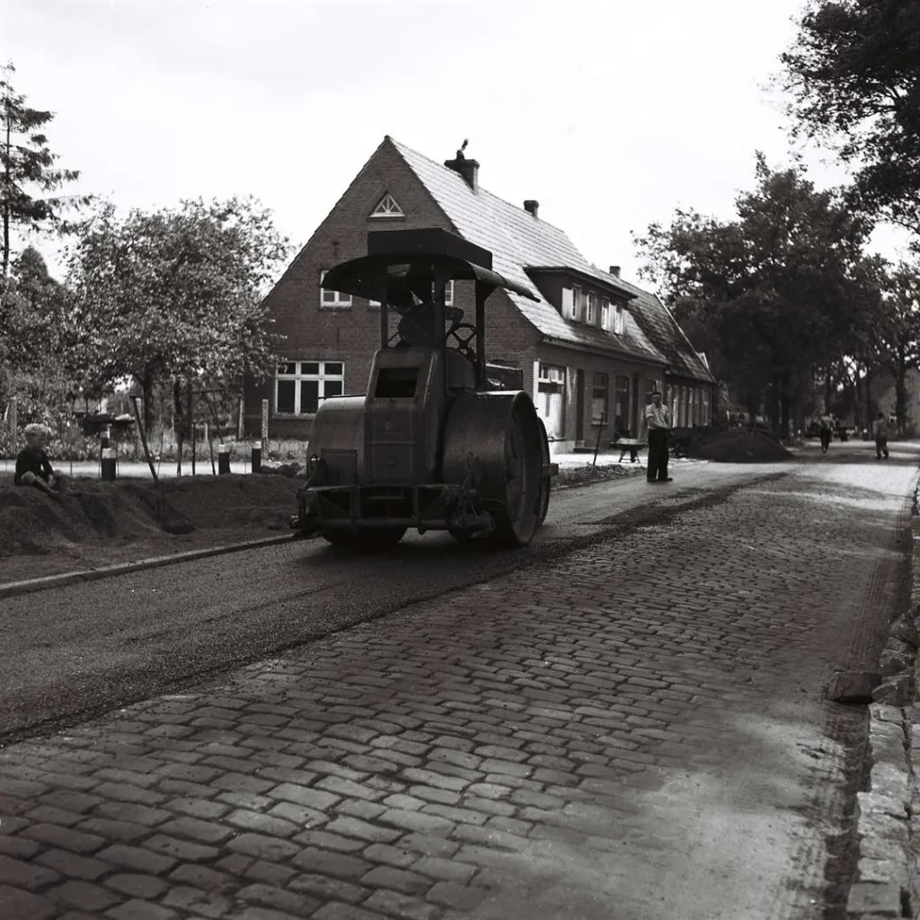 Eine dampfbetriebene Straßenwalze asphaltiert eine Kopfsteinpflasterstraße in einem Dorf der Grafschaft Bentheim.