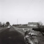 Geparkter Motorroller an einer asphaltierten Landstraße in der Grafschaft Bentheim, im Hintergrund ein fahrendes Auto und ein Bauernhof.