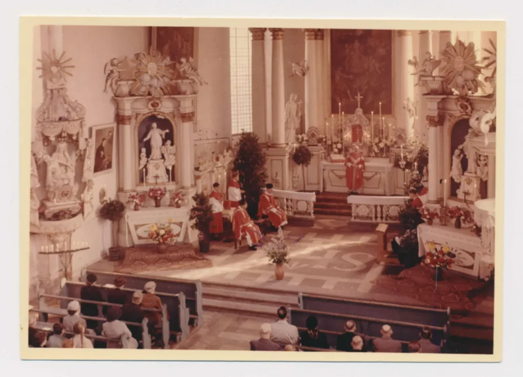 Priester in roten Gewändern zelebrieren einen feierlichen Gottesdienst in einer barocken Kirche vor Gläubigen.