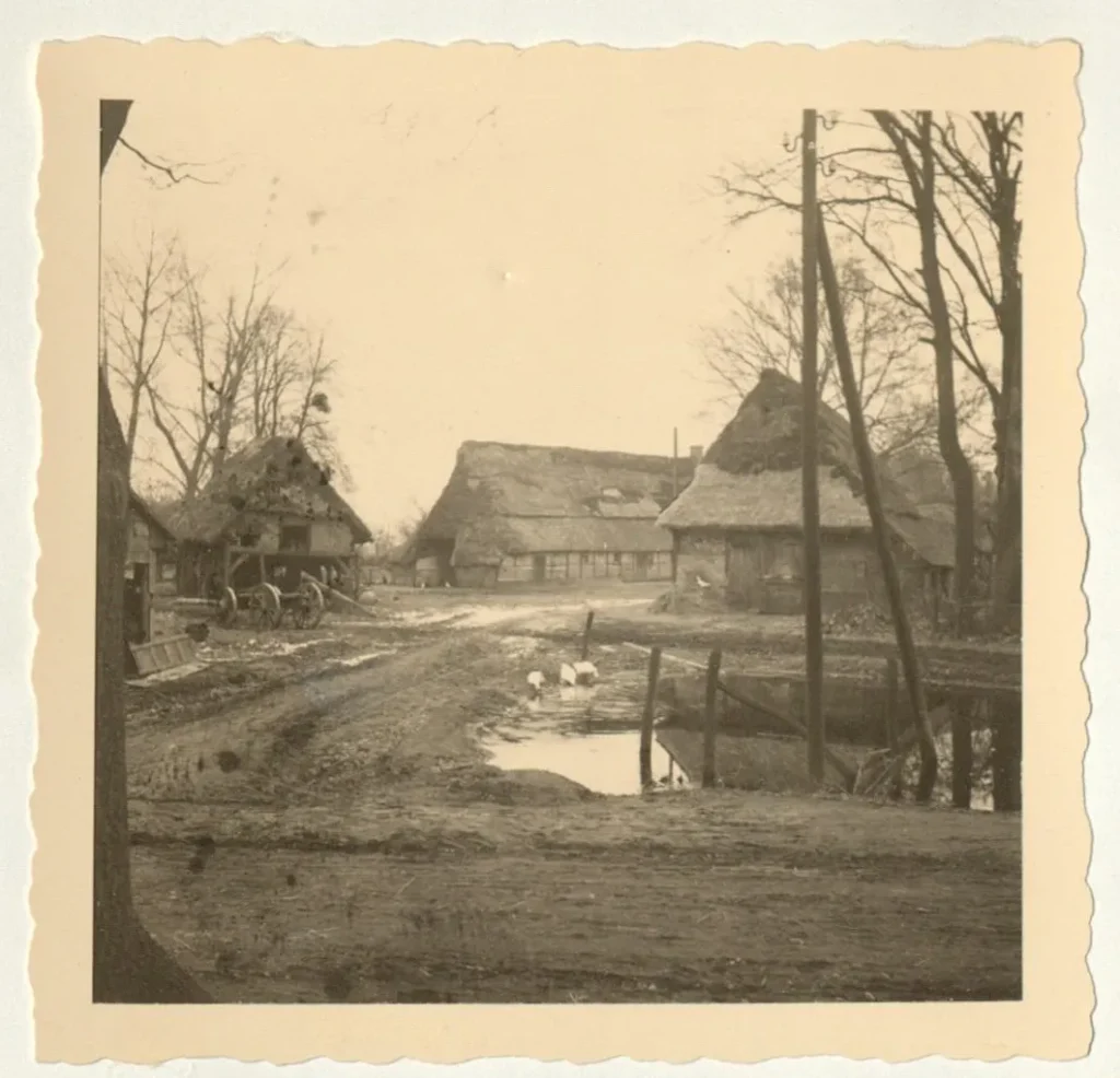 Sepia-Fotografie eines alten Dorfkerns mit strohgedeckten Fachwerkhöfen, Schmutzweg und Ententeich, vermutlich Emsland.