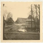 Sepia-Fotografie eines alten Dorfkerns mit strohgedeckten Fachwerkhöfen, Schmutzweg und Ententeich, vermutlich Emsland.