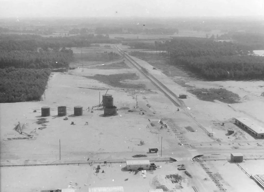 Luftaufnahme der Raffinerie Lingen mit Öltanks, Gleisanlagen und gerodeter Sandfläche, umgeben von Wald, um 1951.