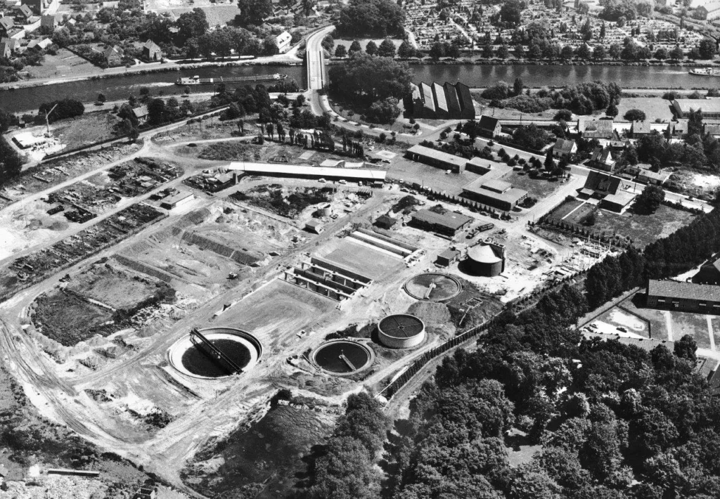 Schwarzweißes Luftbild eines im Bau befindlichen Wasserwerks mit runden Klärbecken und Aufbereitungsanlagen.