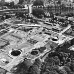 Schwarzweißes Luftbild eines im Bau befindlichen Wasserwerks mit runden Klärbecken und Aufbereitungsanlagen.