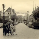 Belebte Straße in Meppen 1951 mit Banner zur Emsland-Ausstellung, Passanten und geparkten Autos der Nachkriegszeit.