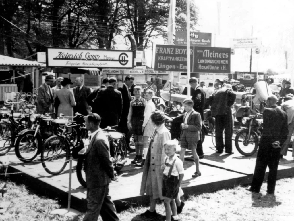 Besucher besichtigen Motorräder auf der Emsland-Ausstellung 1951 in Meppen, im Hintergrund Firmenschilder regionaler Händler.