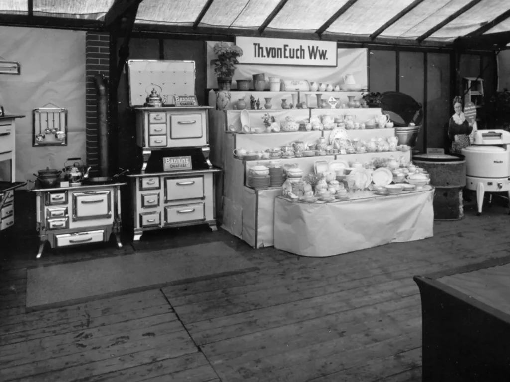 Historischer Messestand mit Küchenherden der Marke Banning und Porzellanwaren unter dem Banner 'Th. von Euch Ww.'