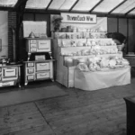 Historischer Messestand mit Küchenherden der Marke Banning und Porzellanwaren unter dem Banner 'Th. von Euch Ww.'