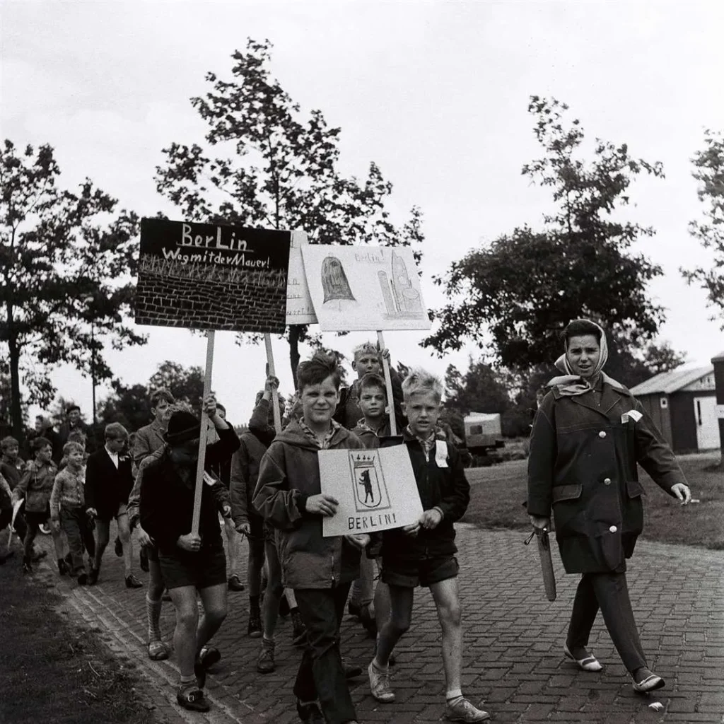 Kinder marschieren mit handgemalten Schildern, darunter 'Berlin – Weg mit der Mauer', bei der Bohrturmwanderung 1961.