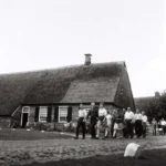 Gruppe von Menschen spaziert auf gepflastertem Weg vor einem reetgedeckten niederländischen Bauernhaus, ca. 1961.