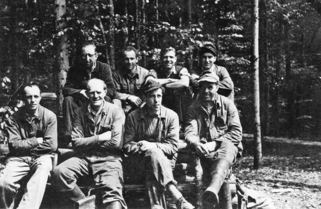 Acht Männer in Arbeitskleidung posieren für ein Gruppenfoto im Wald, vermutlich Mitarbeiter der Deutschen Schachtbau.