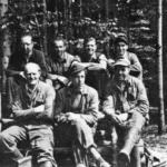 Acht Männer in Arbeitskleidung posieren für ein Gruppenfoto im Wald, vermutlich Mitarbeiter der Deutschen Schachtbau.