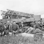 Gruppe von Arbeitern rastet im Gras vor Bohrfahrzeugen auf einem Erdölfeld im Emsland.