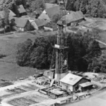 Luftaufnahme eines Erdölbohrturms mit Industrieanlagen, umgeben von Feldern und Bauernhöfen im Emsland.