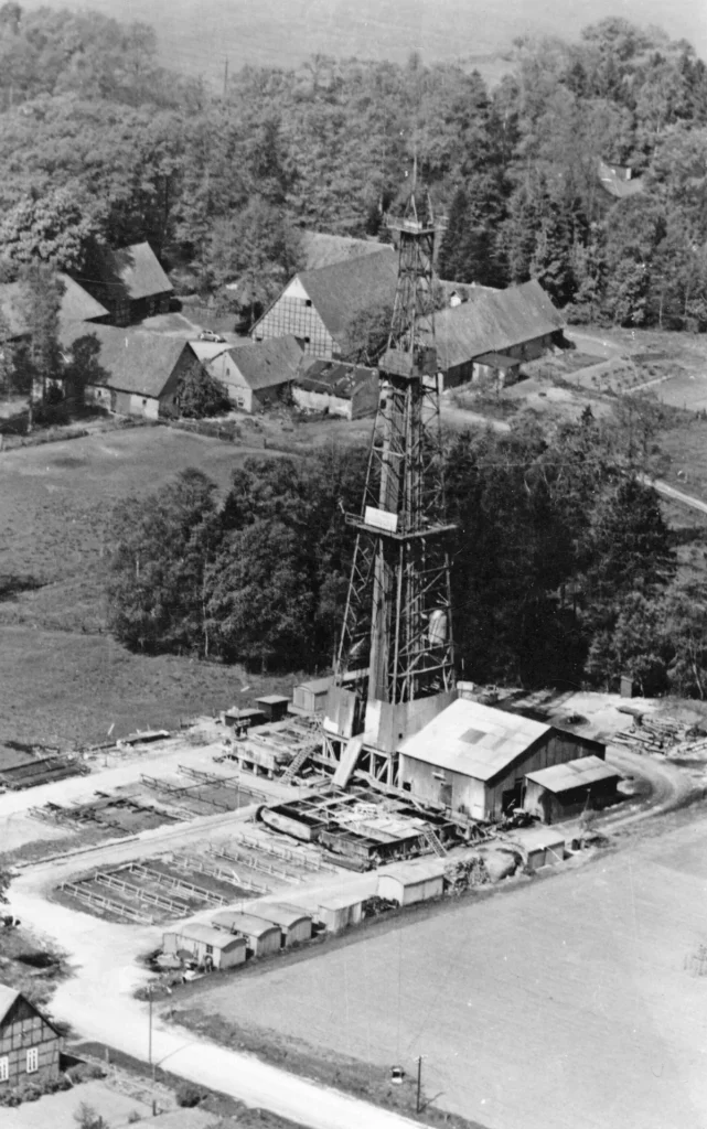 Luftaufnahme eines Erdölbohrturms mit Industrieanlagen, umgeben von Feldern und Bauernhöfen im Emsland.