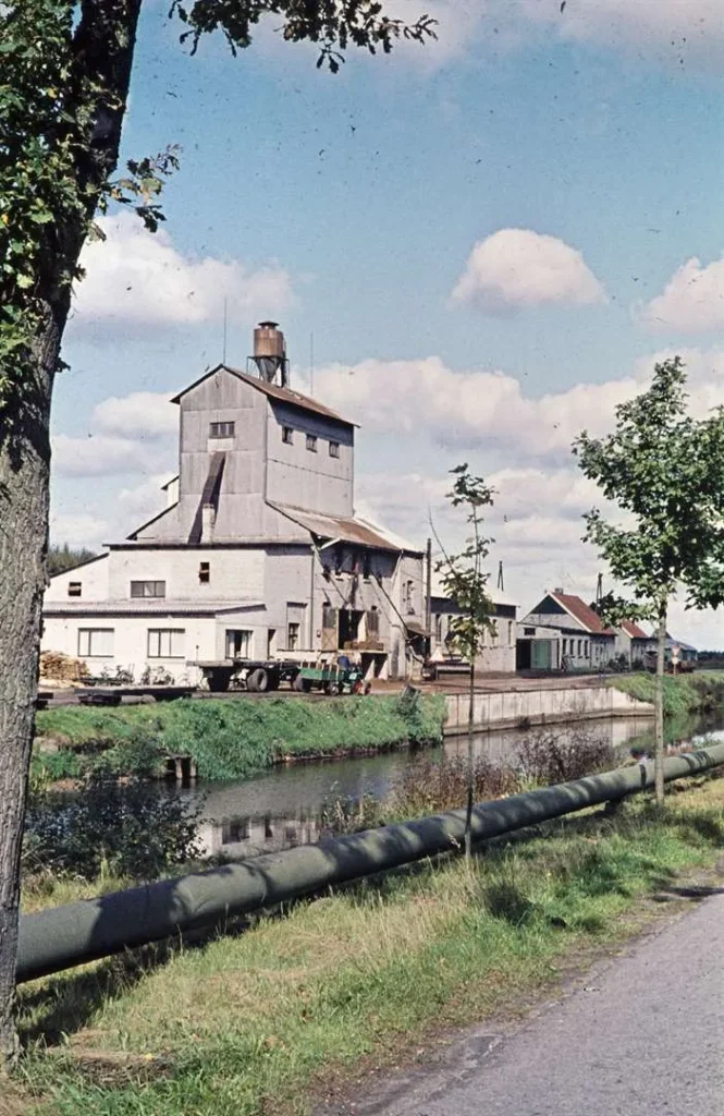 Historische Torfverarbeitungsanlage mit Förderturm an einem Kanal, umgeben von Grünflächen und Wirtschaftsgebäuden.