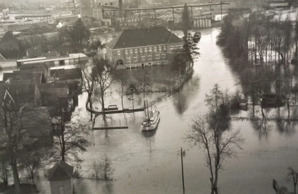Luftaufnahme einer überfluteten Stadt mit einem Boot zwischen Gebäuden und Bäumen, vermutlich Nordhorn bei Vechte-Hochwasser.