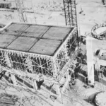 Luftaufnahme des Rohbaus der Raffinerie Lingen mit Stahlbeton-Fundament, Gerüsten und Kränen auf Sandfläche.