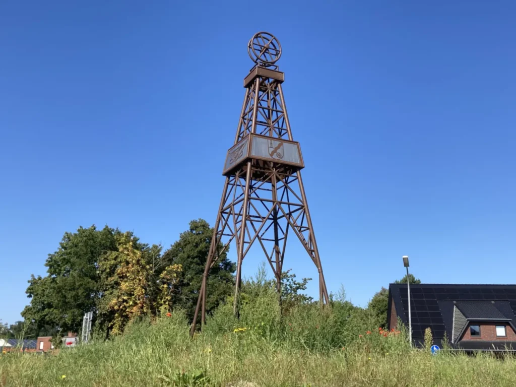 Rostbrauner Stahlbohrturm mit Förderrad als Denkmal am Kreisverkehr in Dalum vor blauem Himmel.