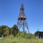 Rostbrauner Stahlbohrturm mit Förderrad als Denkmal am Kreisverkehr in Dalum vor blauem Himmel.